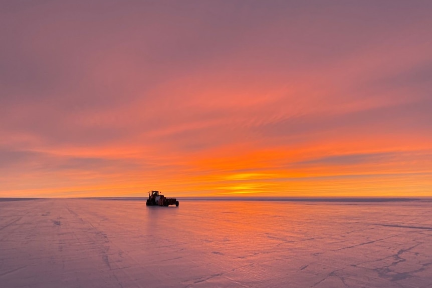 Wide shot of a tractor on ice at sunrise