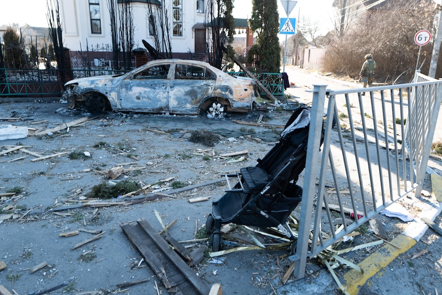 A burnt out car and pram are abandoned by the road