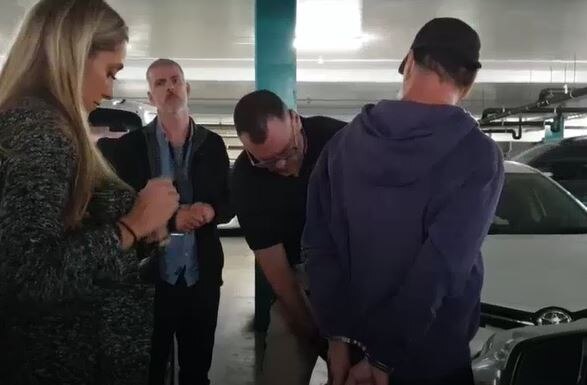 Police arresting a man, whose face is blurred, in a car park.