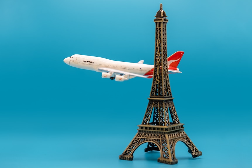 A photo of a miniature plane flying past an Eiffel tower.