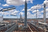 Industrial looking processing plant in front of red dirt and blue sky.