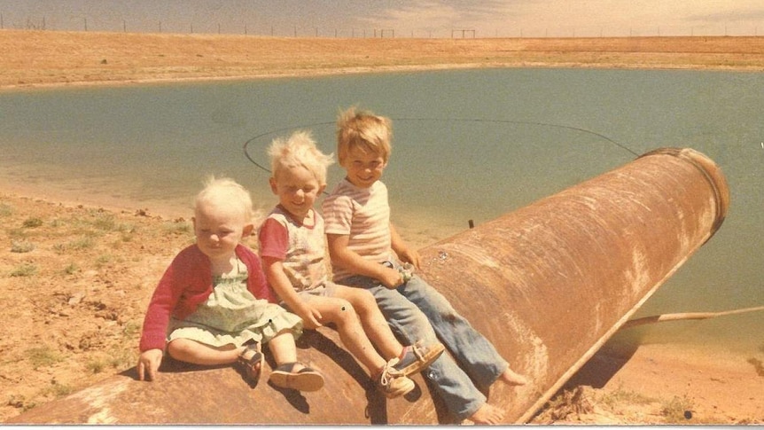 Three children sit on a pipe near a dam.