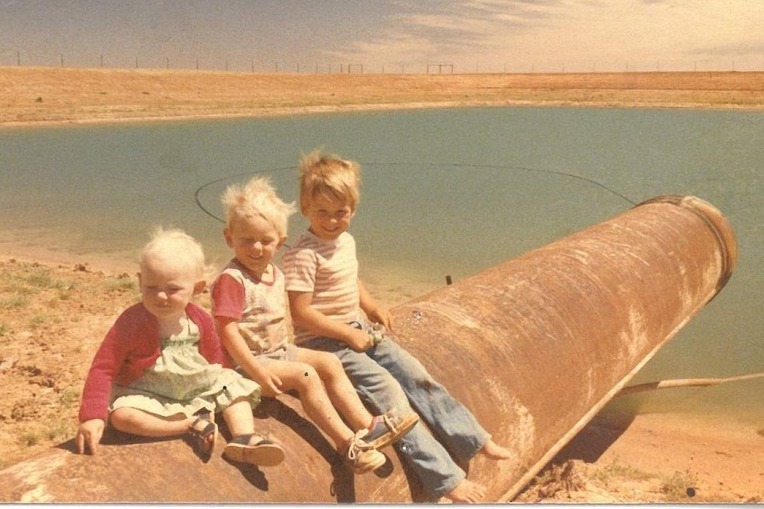 Three children sit on a pipe near a dam.