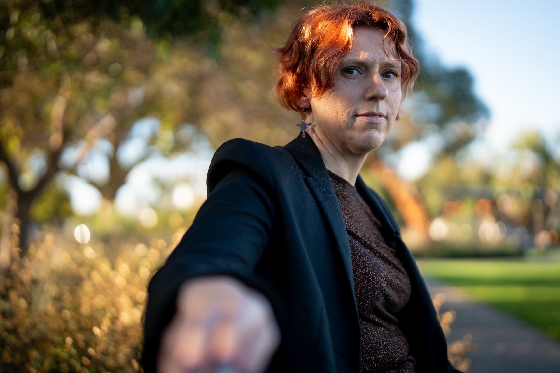 A low angle of a woman with short red hair, who sits on a park bench