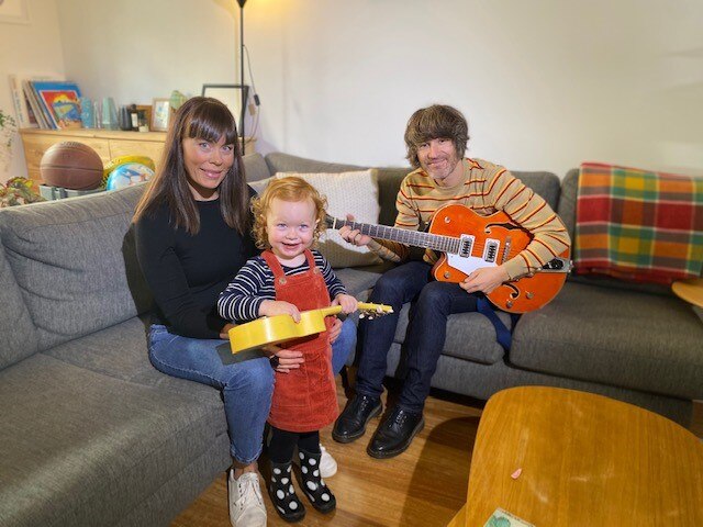 Kate Goldby and Zac Anthony sit on the couch in their home with their daughter Lola.