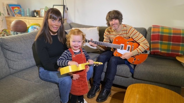 Kate Goldby and Zac Anthony sit on the couch in their home with their daughter Lola.