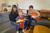 Kate Goldby and Zac Anthony sit on the couch in their home with their daughter Lola.