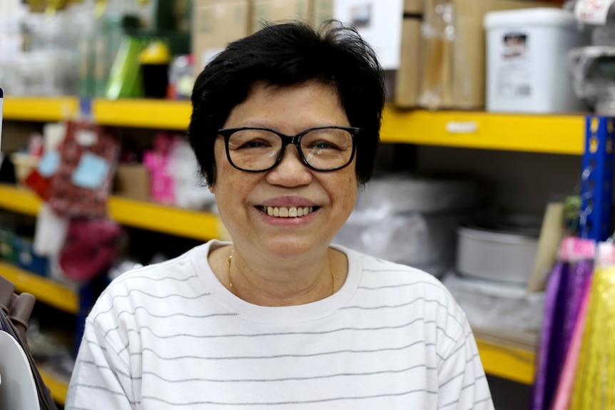 Hong Peng Yen smiles as she stands in front of a shelf of dessert supplies inside her store.