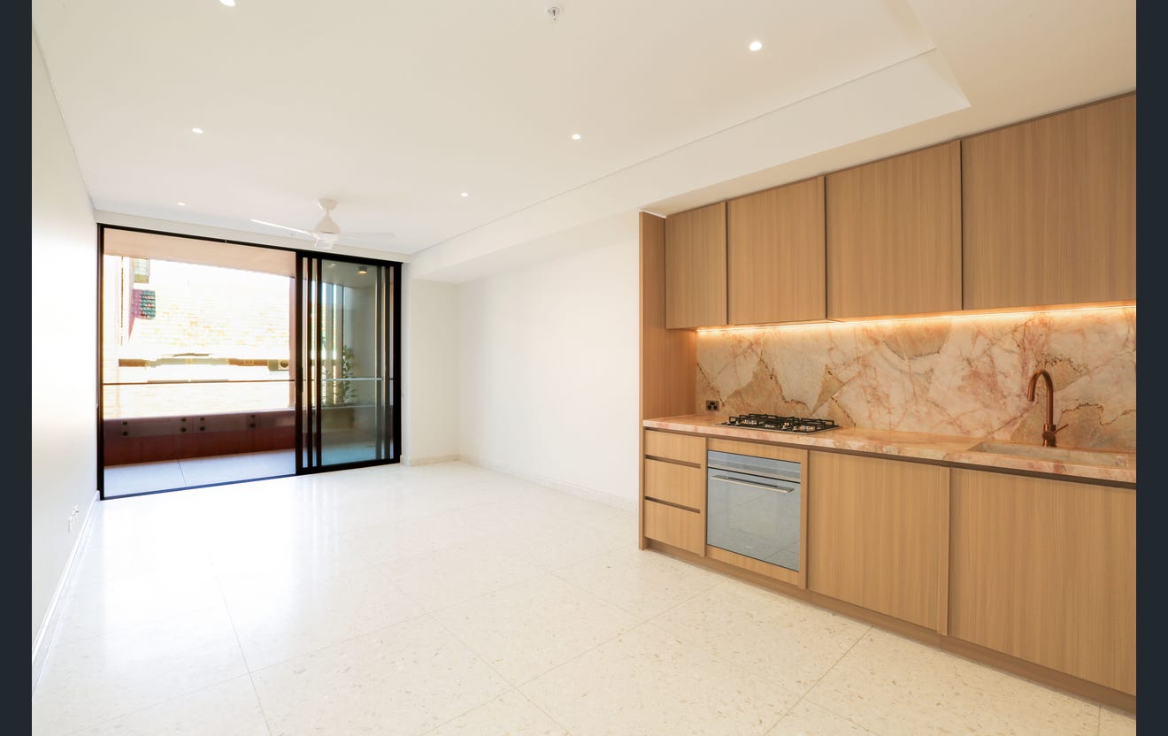 A real estate photo shows a modern galley kitchen opening on to a vacant living area.