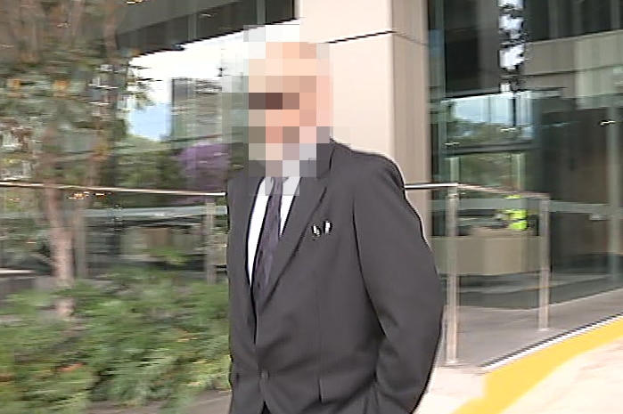A man in a suit with a pixelated face walks in front of an office building.