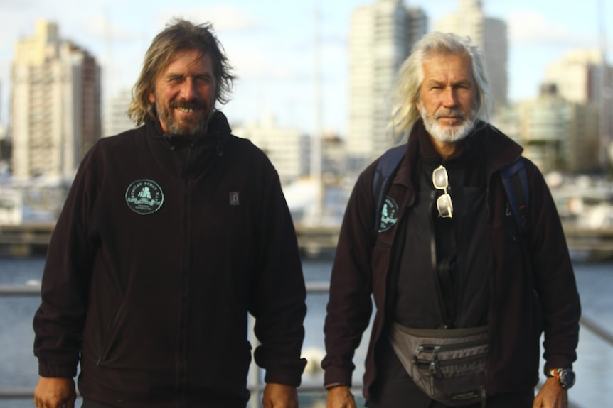 Two men look at the camera. They are standing on land.