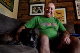 A man in a green shirt on a couch next to a dog, smiling.
