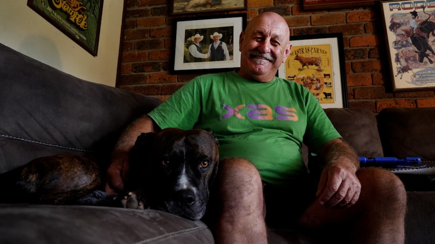 A man in a green shirt on a couch next to a dog, smiling.