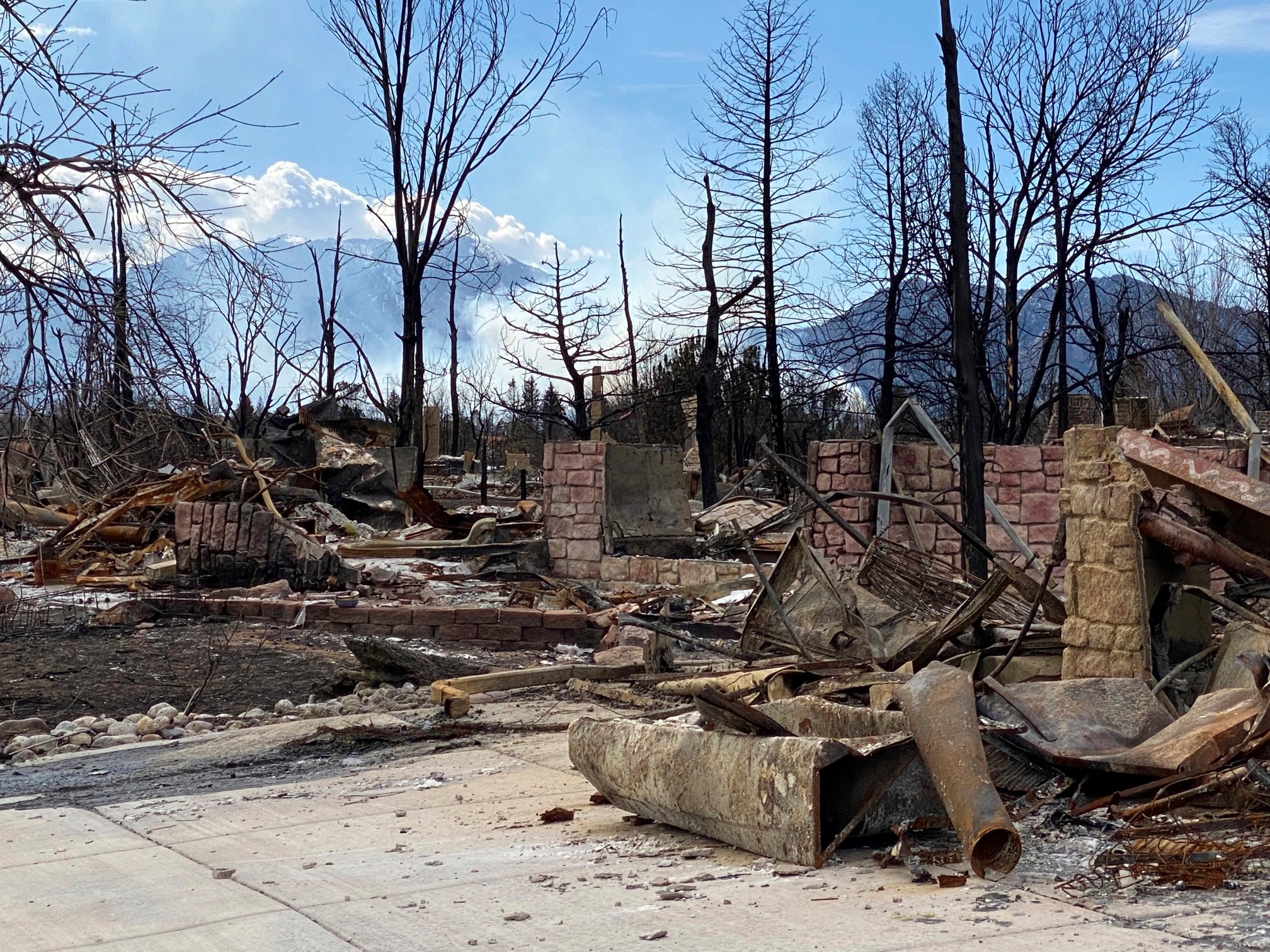 A burnt out house with smoke from a fire burning in the background