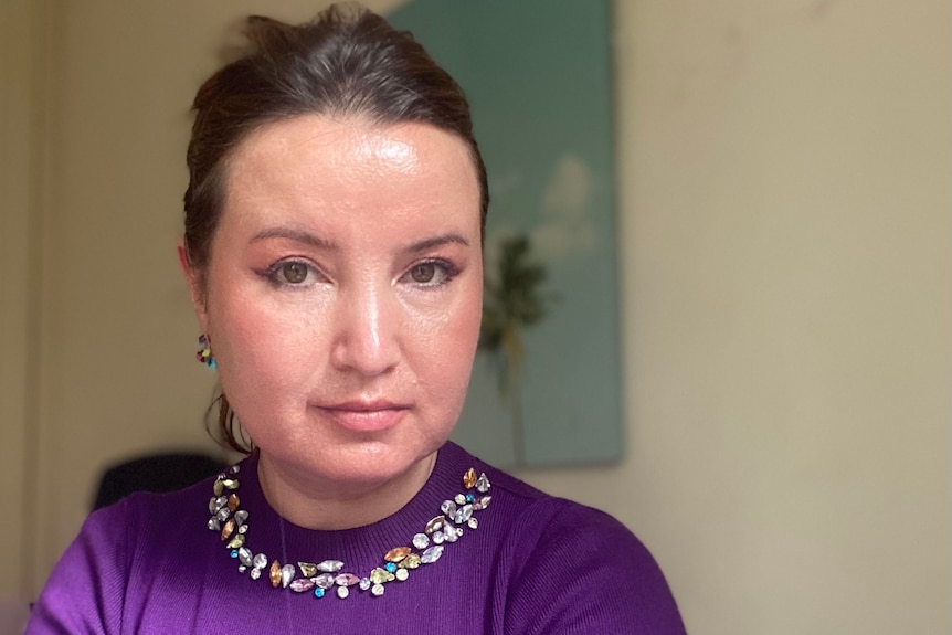 A photo of a woman in a purple top with jewelled neckline.