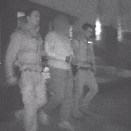 A grainy photo shows police leading a member of the Hells Angels outlaw bikie club away in handcuffs.