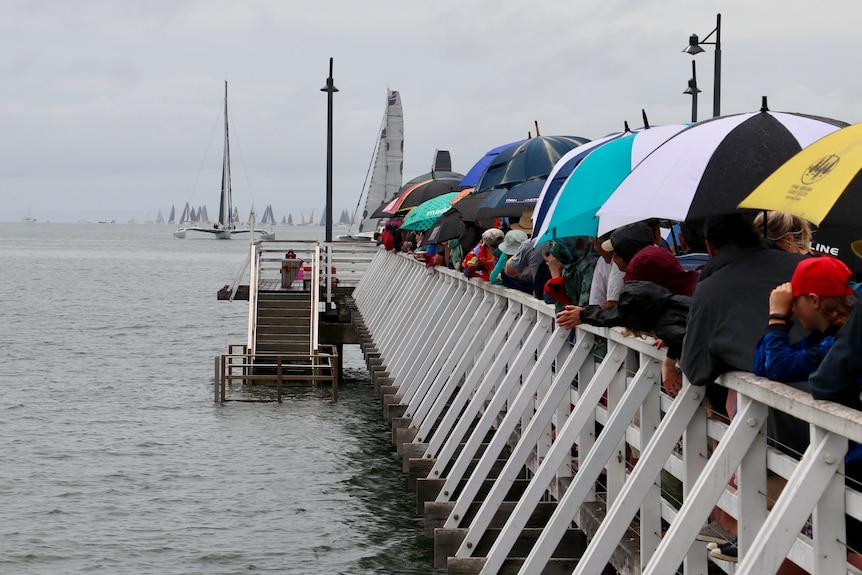 a crowd of people packed onto a pier in grey rainy conditions with lots of umbrellas