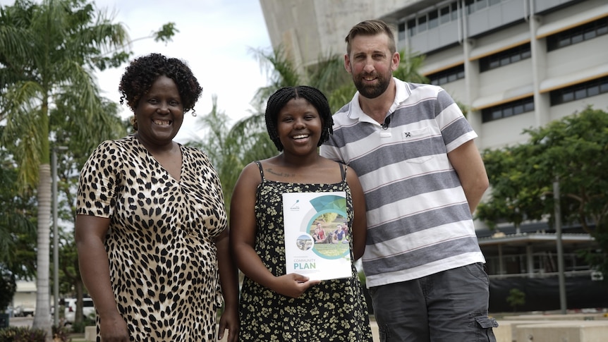 Two women and a man hold a council document. 