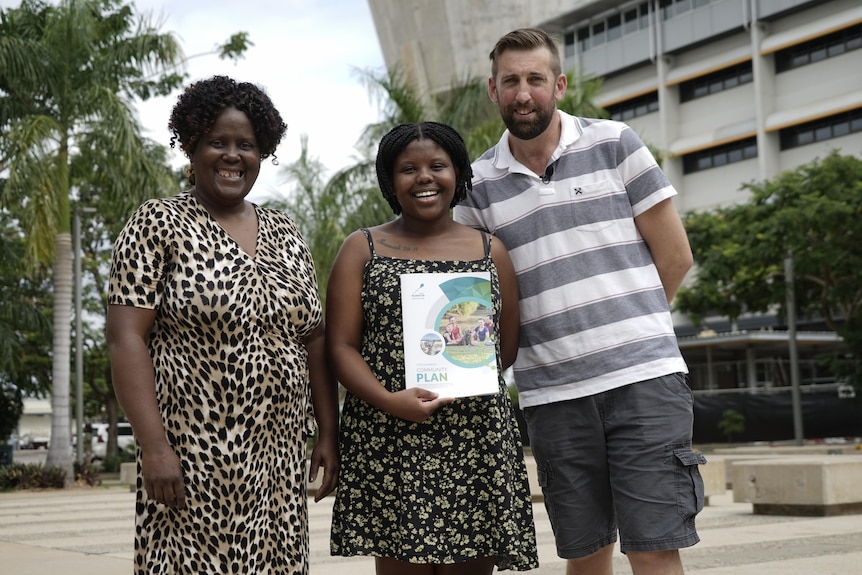 Two women and a man hold a council document. 