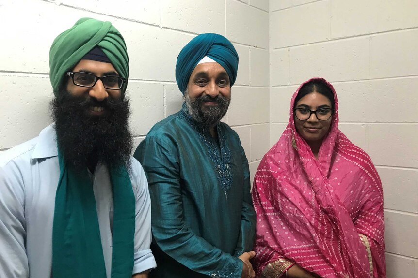 Two Indian men with turbans and beards and a young Indian woman, all wearing brightly coloured clothes smiling at the camera.