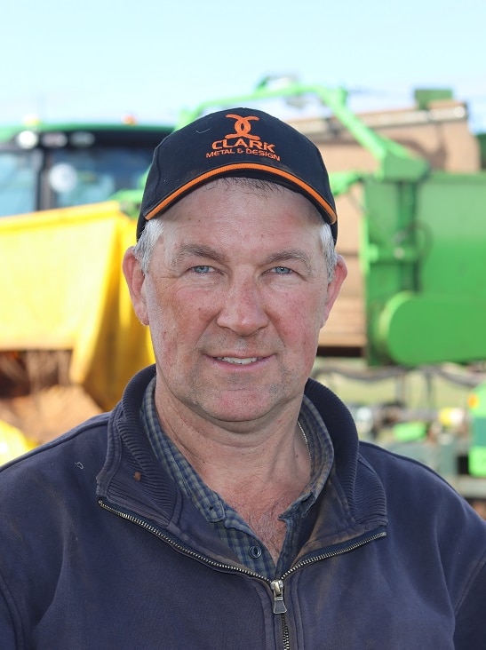 A man stands in front of a potato harvester.