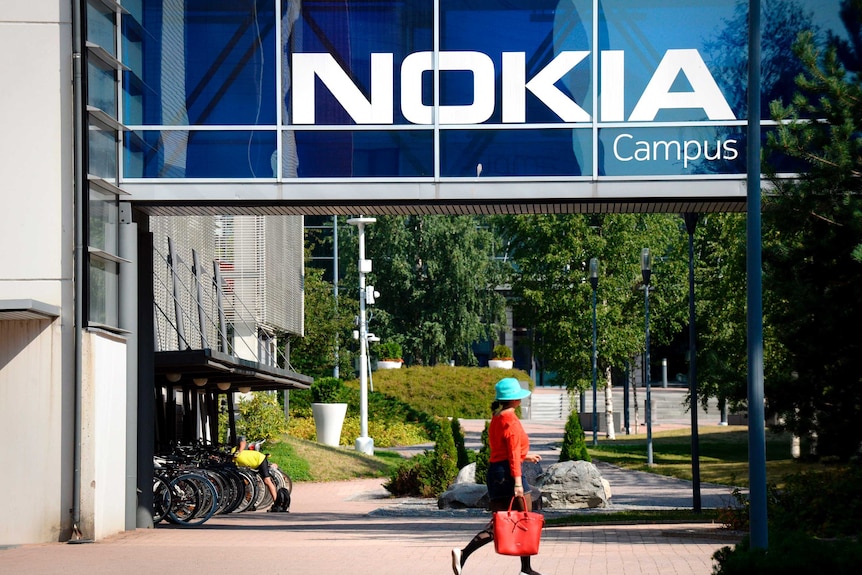 A woman wearing a red shirt walks in front of a sign saying 'Nokia campus'