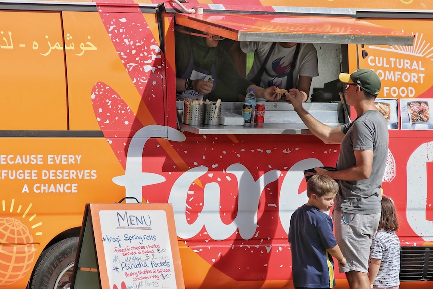 A man and two small children stand at a red and orange food truck ordering food.
