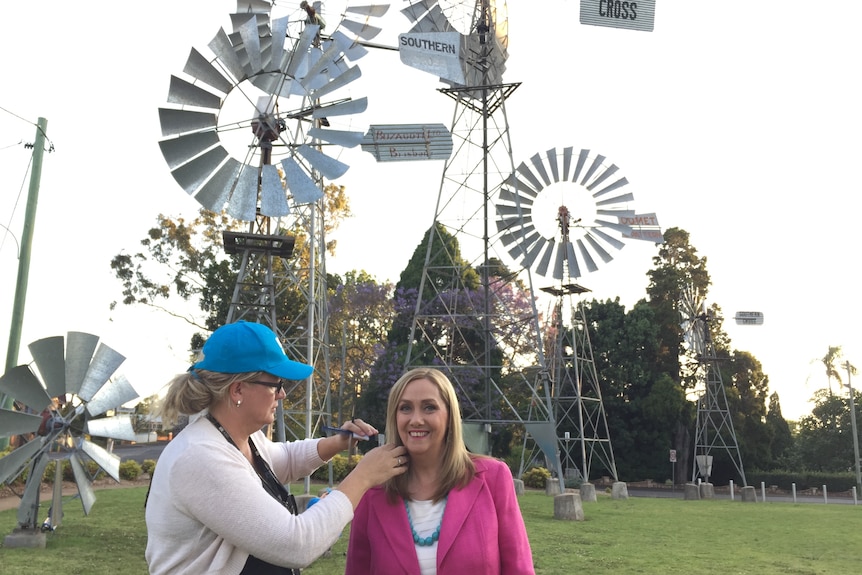 Woman fixing earpiece to another woman standing in front of windmills.