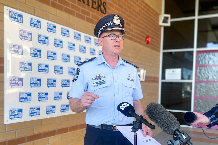 A policeman in uniform stands in front of media microphones