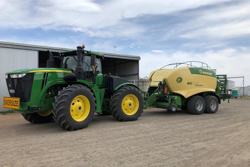 A brand new green-and-yellow tractor and hay baler outside a shed