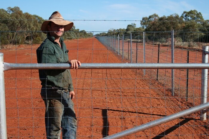 Farmer Dean Hague standing next to a high fence capable of keeping kangaroos off his property.