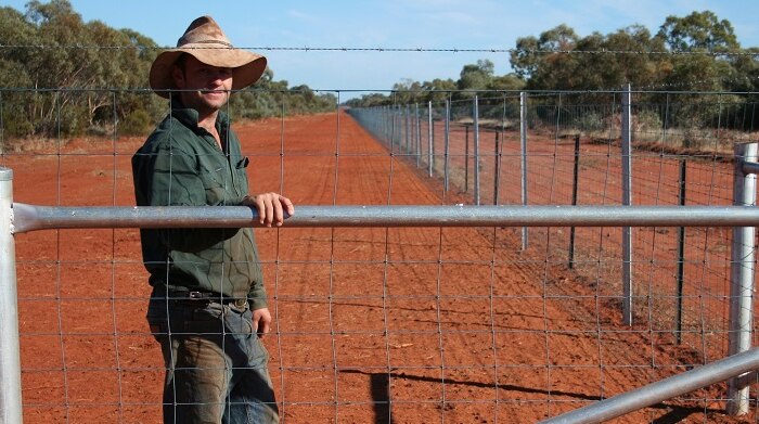Farmer Dean Hague standing next to a high fence capable of keeping kangaroos off his property.