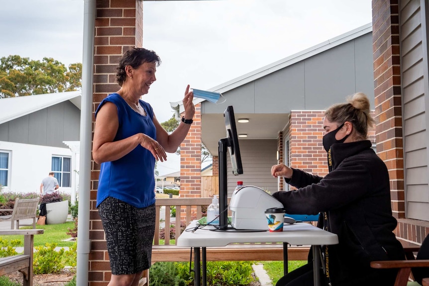 Angela Raguz at an aged care concierge desk getting a COVID-19 mask.