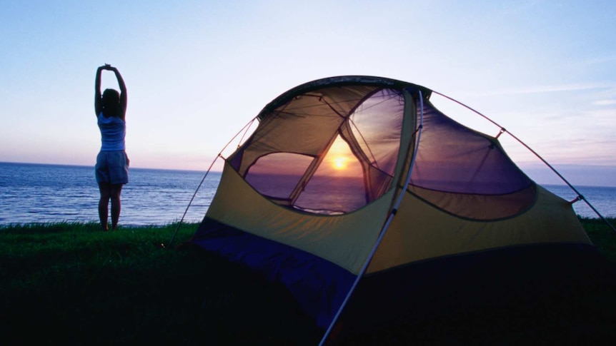 Person stretching outside tent at dawn