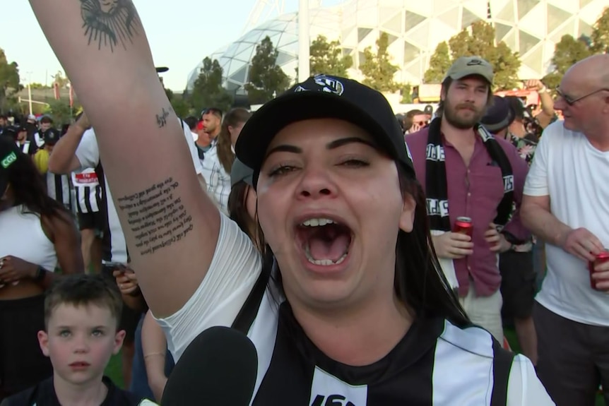 A woman in Collingwood clothing shouts and raises her arm.