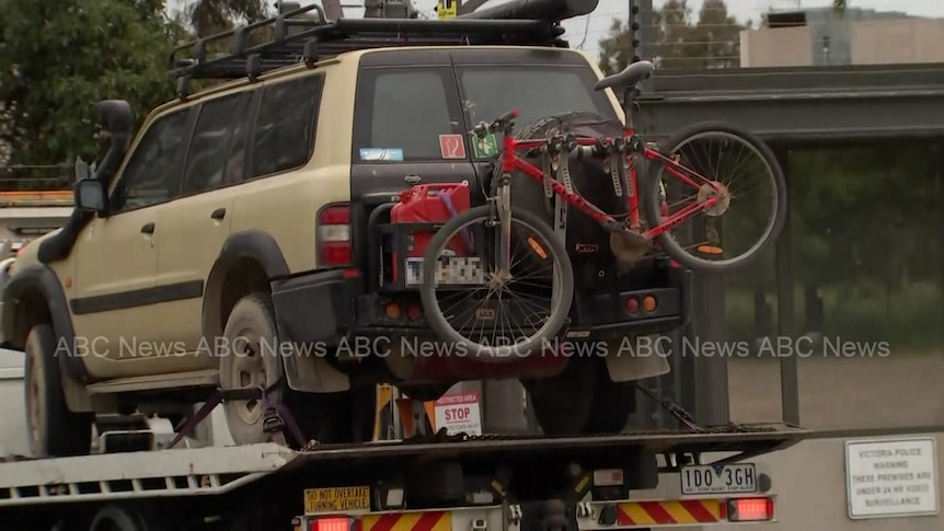 A light-coloured 4WD with a bicycle loaded on the back of a truck