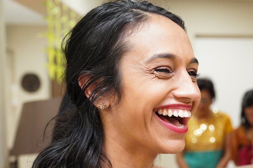 Tasha wearing a vibrant saree and laughing in the image.