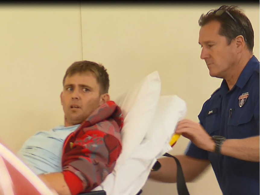 A man lying on an ambulance stretcher is pushed into hospital by a paramedic.