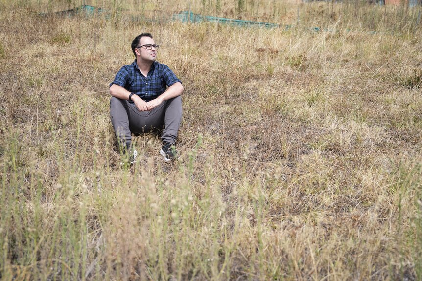 Un hombre está sentado en un campo vacío de hierba alta y seca.