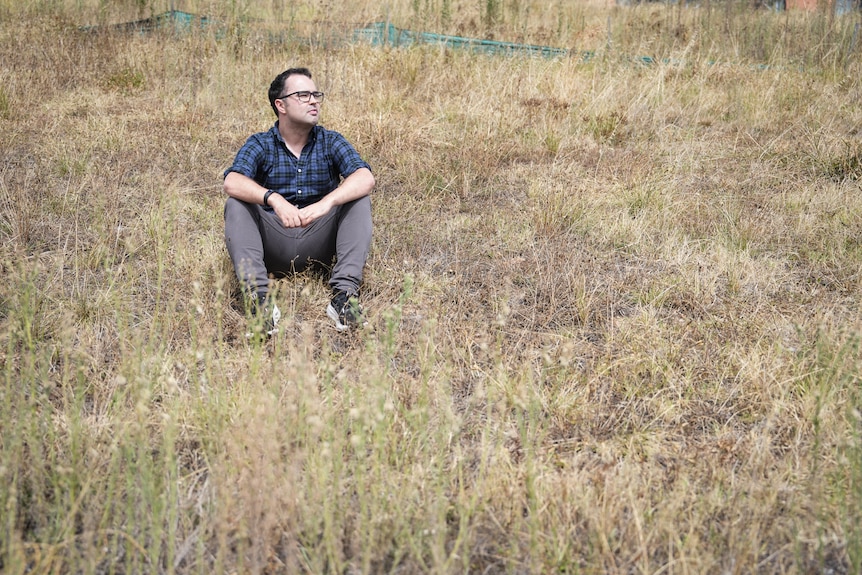 A man sits in an empty field of tall, dry grass.
