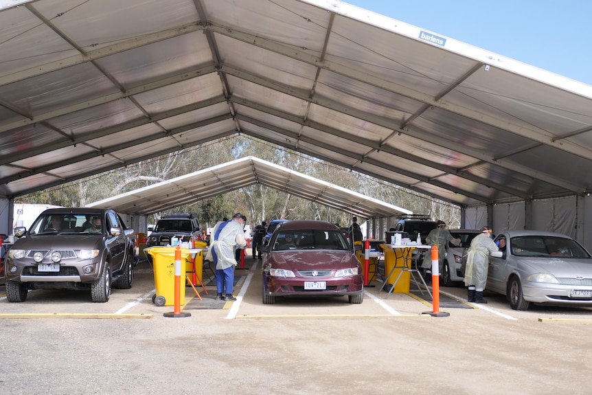 three rows of cars driving through tent with nurses in PPE conducting swabs