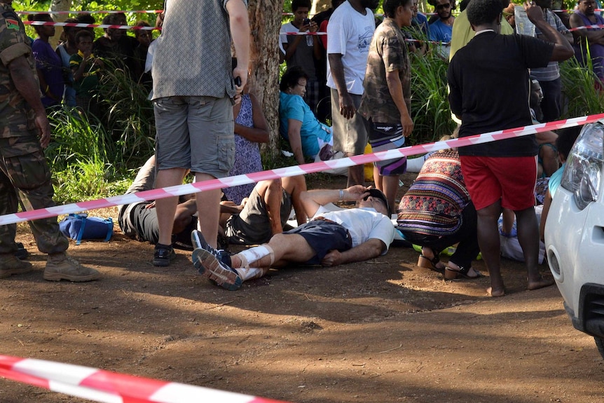 View through police tape of people lying on the ground as emergency services assist them.