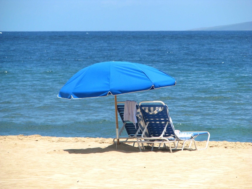 Two lounges sit under a beach umbrella at the beach.