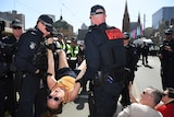 Police carry a woman by her arms and legs, while other officers watch on.