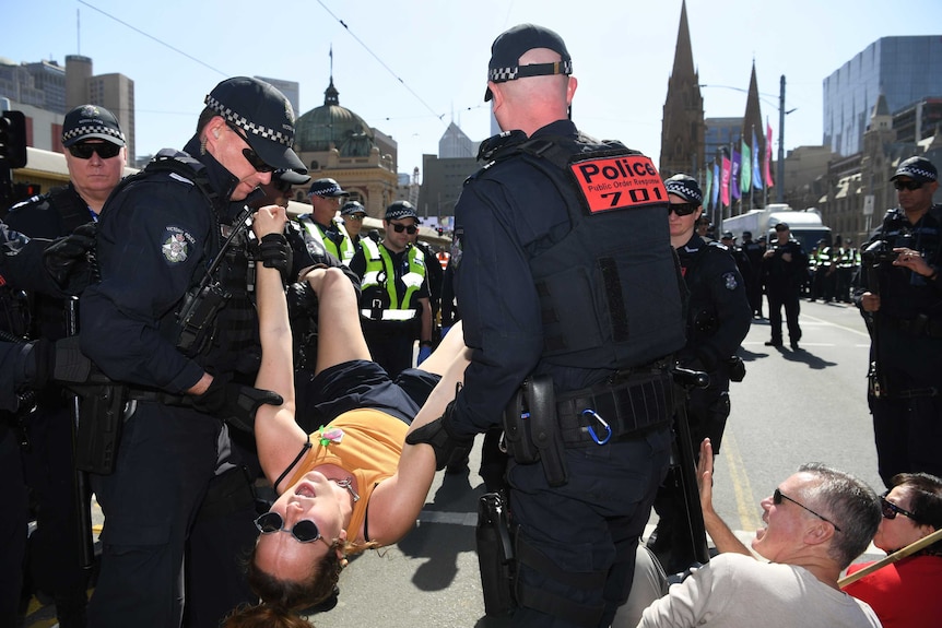 Police carry a woman by her arms and legs, while other officers watch on.