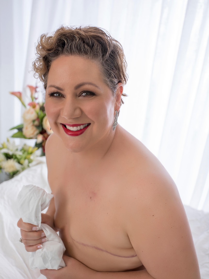 A portrait of a topless woman who has had her breasts removed smiling at camera 