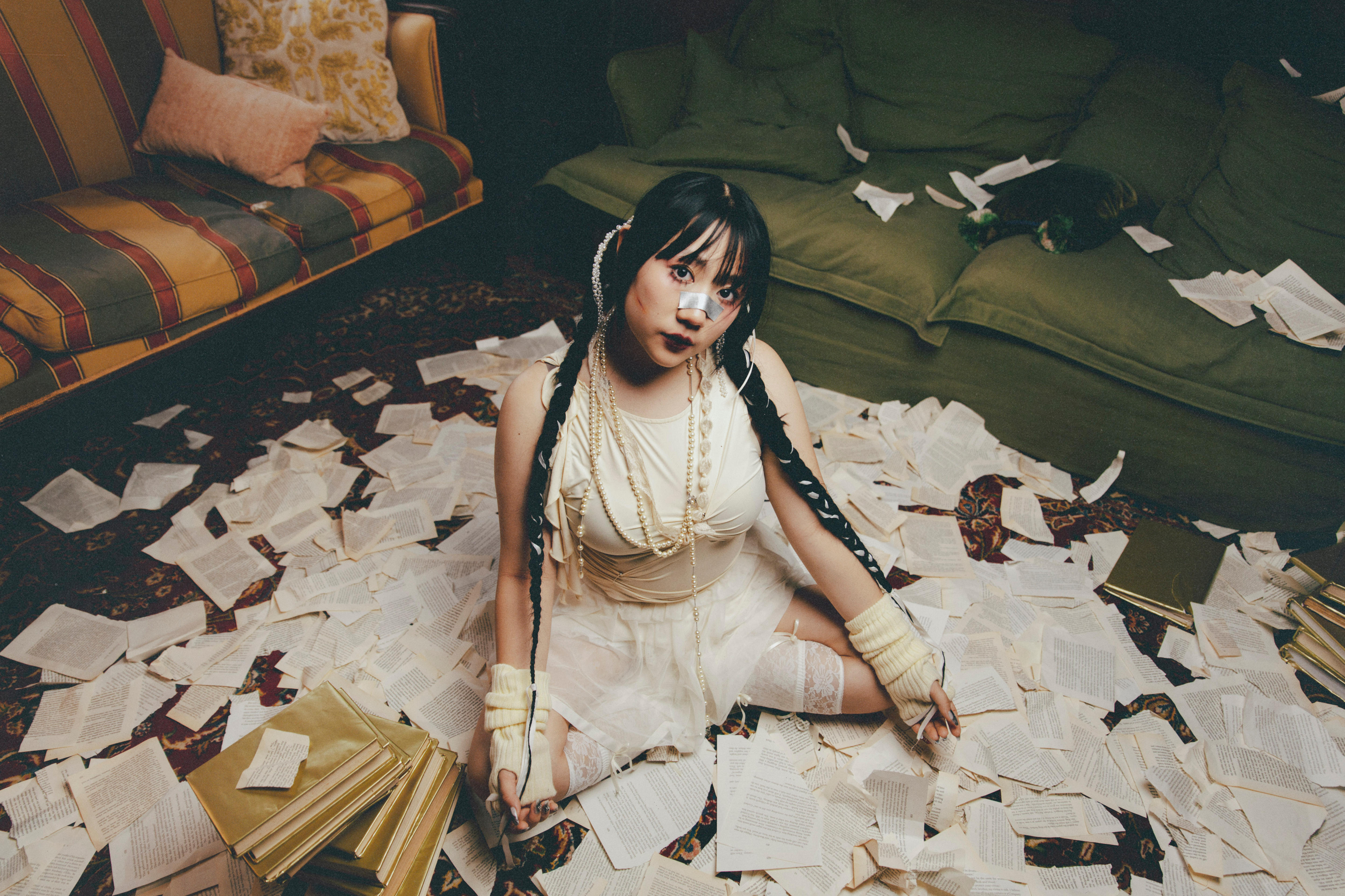 A woman sits on the floor in a white lace dress with book pages scattered around her