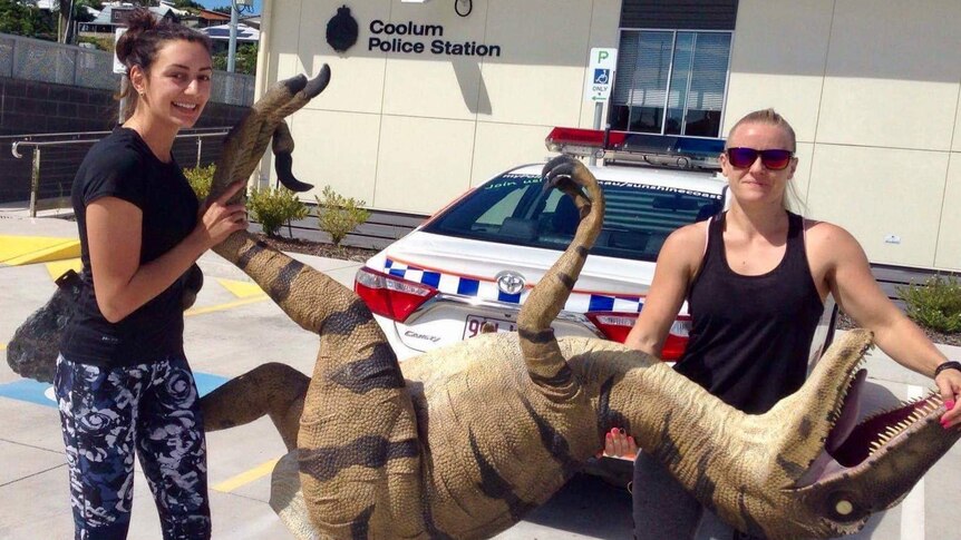 two women hold the dinosaur outside the police station