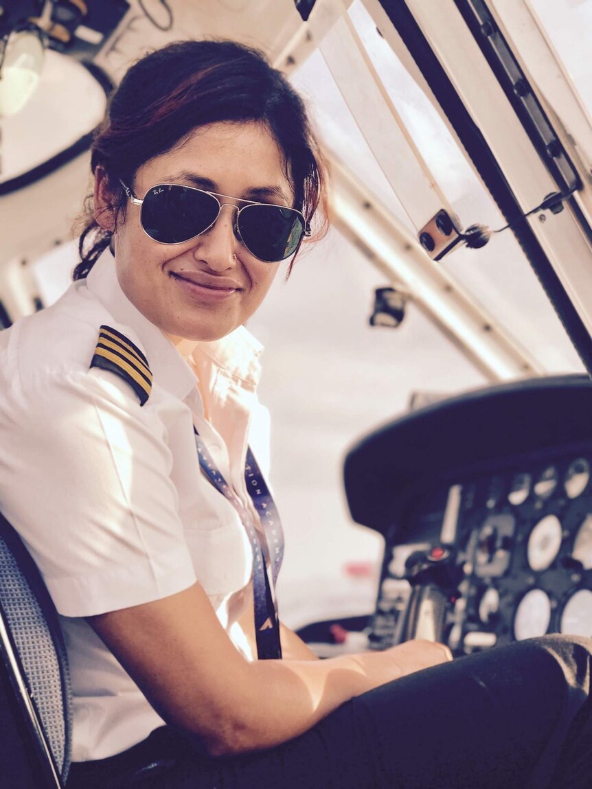 Female helicopter pilot sitting in the cockpit smiling.