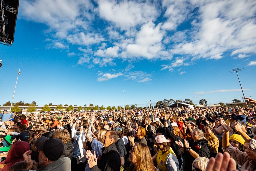 A large music festival crowd beneath a sunny sky.